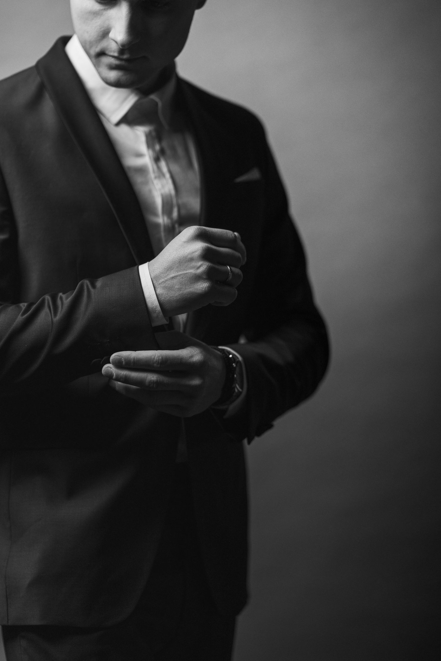 Black and white photo of a man in suit adjusting his cufflinks. γαμπρός