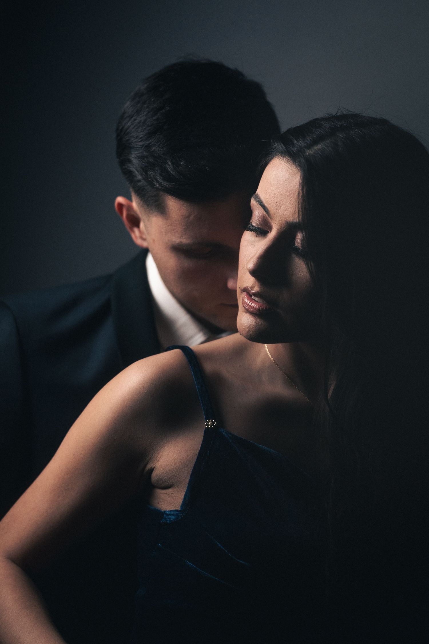 Moody portrait of a couple in formal attire against dark background.