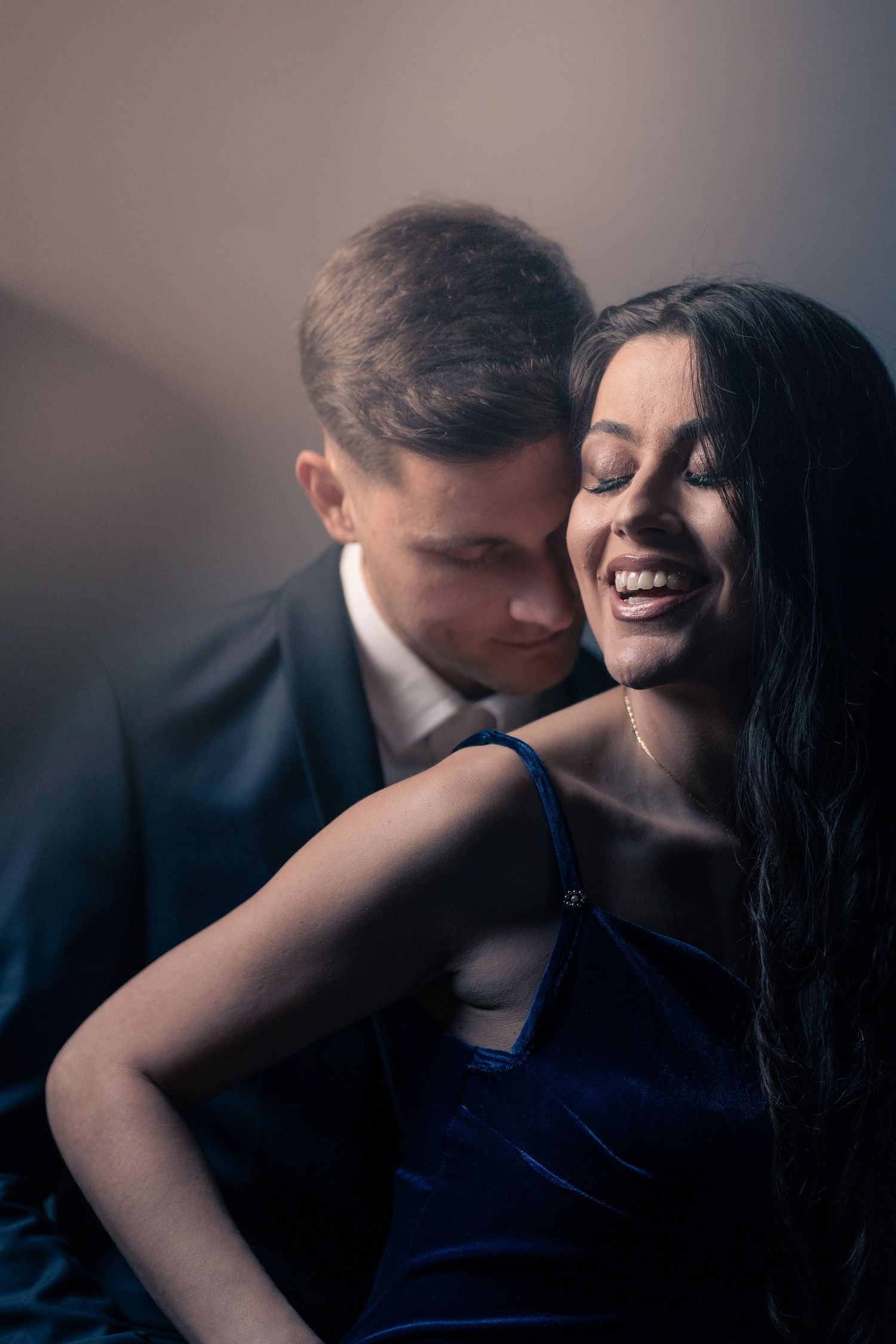 Intimate portrait of a couple sharing a joyful moment in blue evening attire.