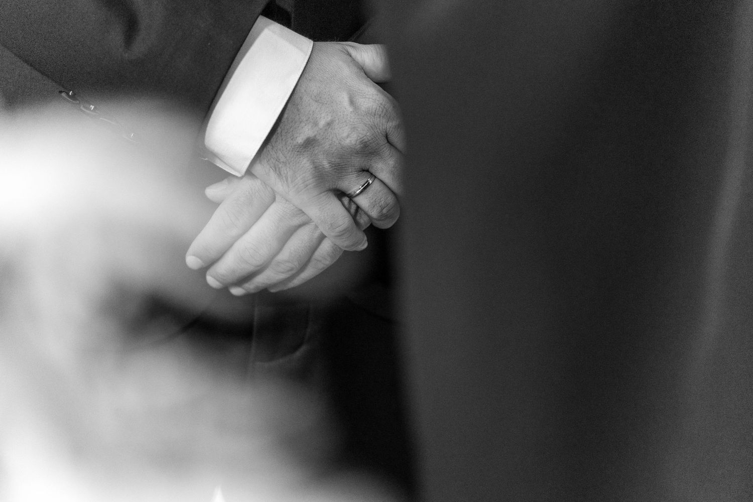 Black and white close-up of clasped hands showing wedding rings.