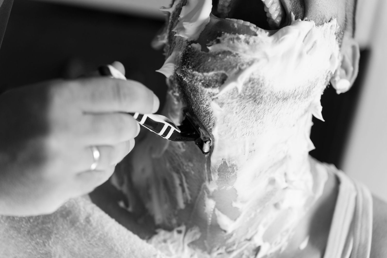 Close-up black and white image of someone getting a traditional straight razor shave.