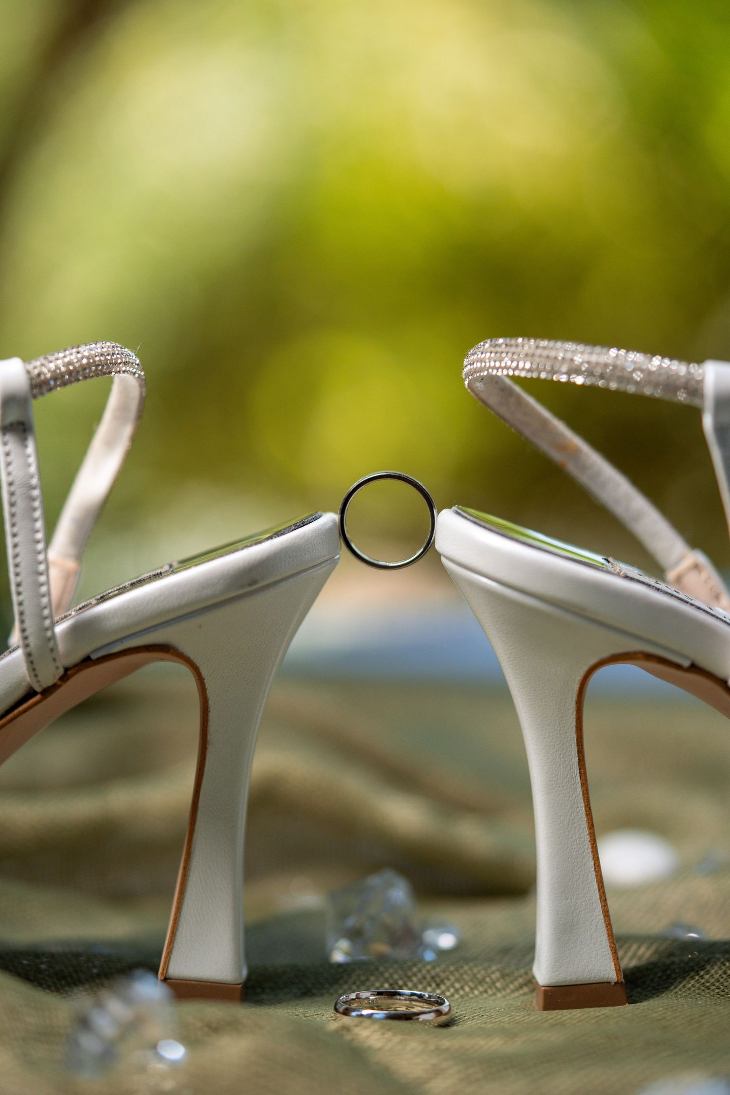 Wedding ring positioned between white bridal shoes with sparkly straps. Φωτογραφος γάμου Αθήνα.