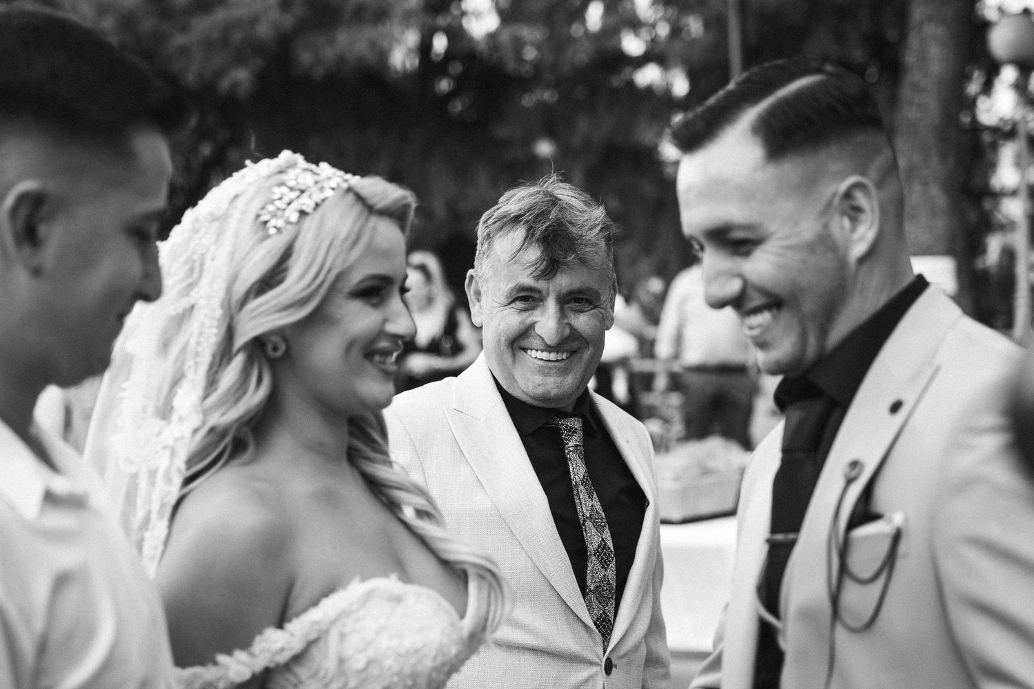 Black and white candid photo of wedding guests sharing joyful moments during an outdoor celebration.