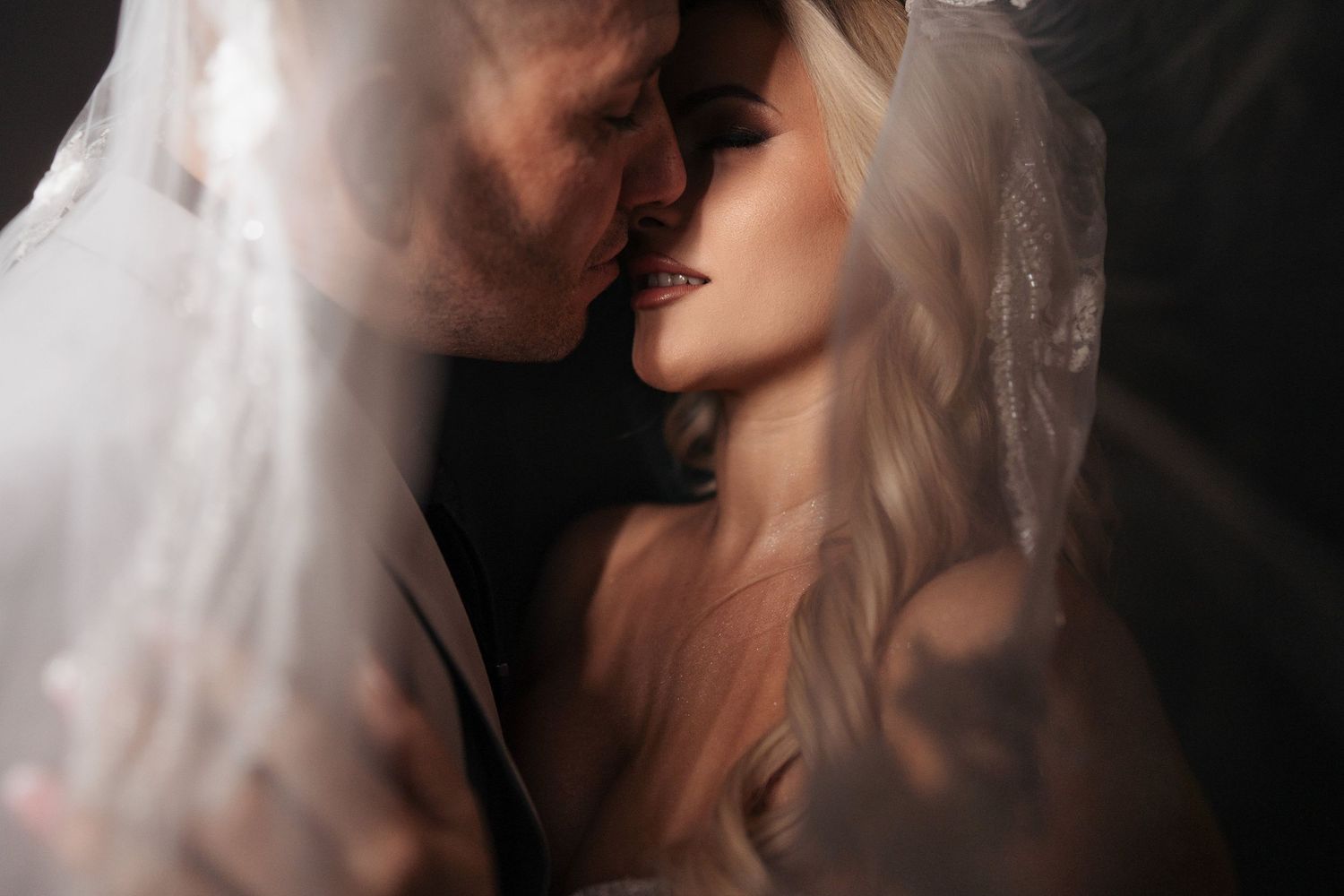 Romantic black and white portrait of a couple in an intimate moment with soft lighting and shadows.