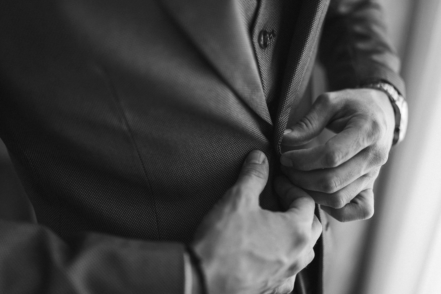 Close-up black and white photo of hands adjusting a suit jacket sleeve and cuff link.