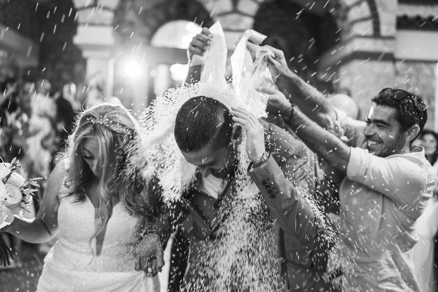 Wedding celebration with guests dancing and throwing water in dramatic party lighting.