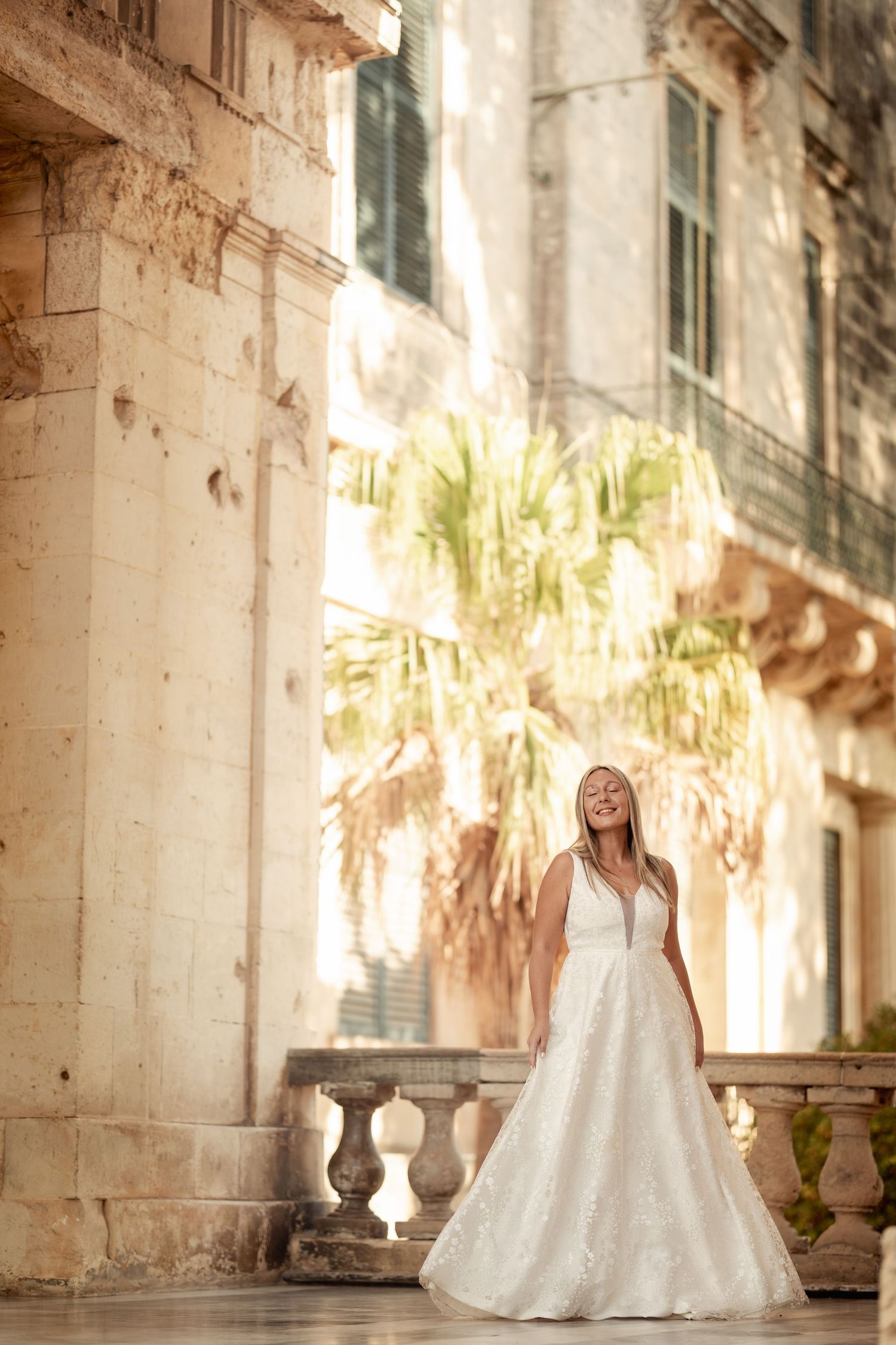 A bride in a flowing white wedding gown poses and twirls in a series of joyful shots against a sunlit stone building.