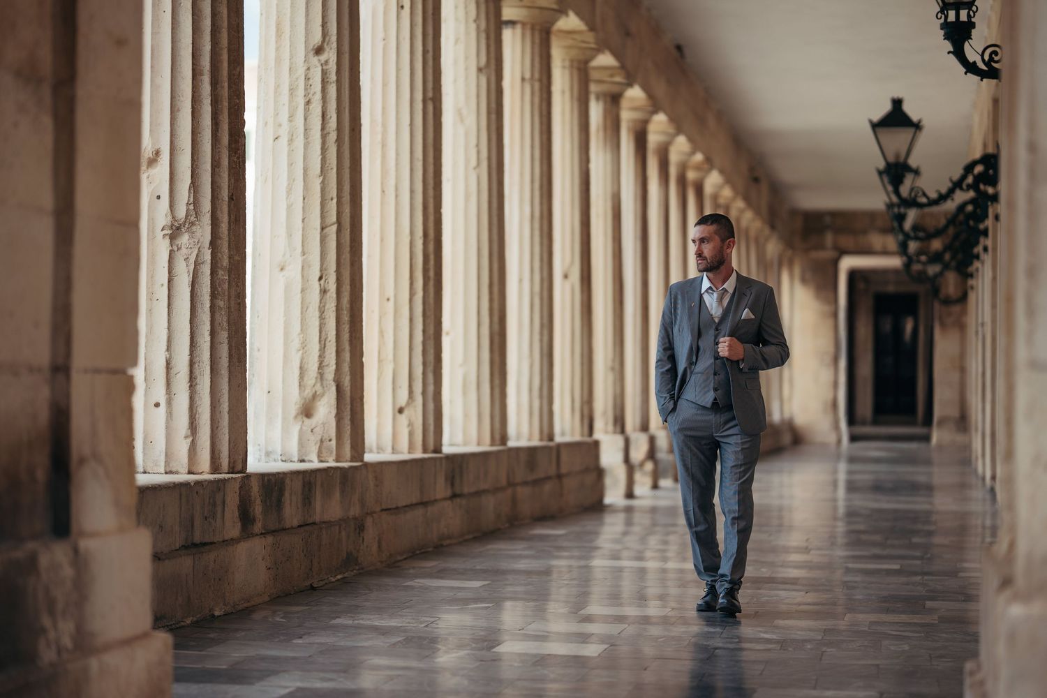 Long stone colonnade hallway with arched pillars and natural lighting streaming through windows.