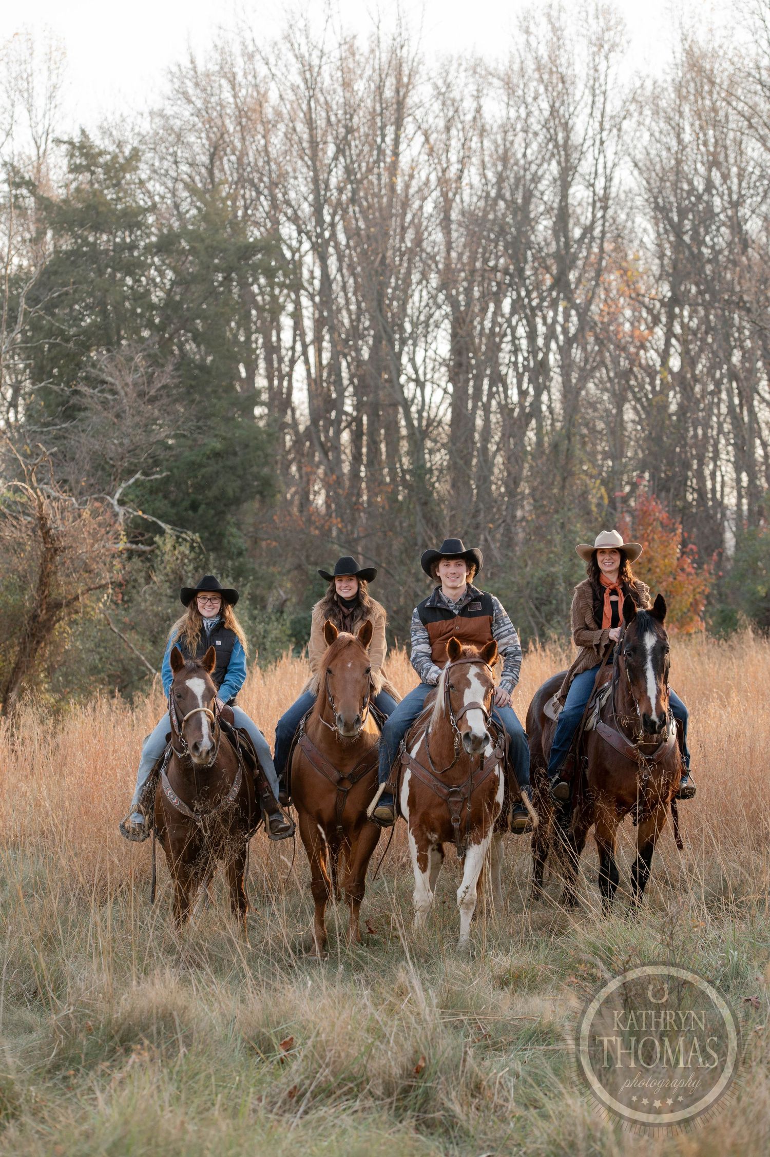 Group of four riders on horseback in traditional western attire against autumn forest background.