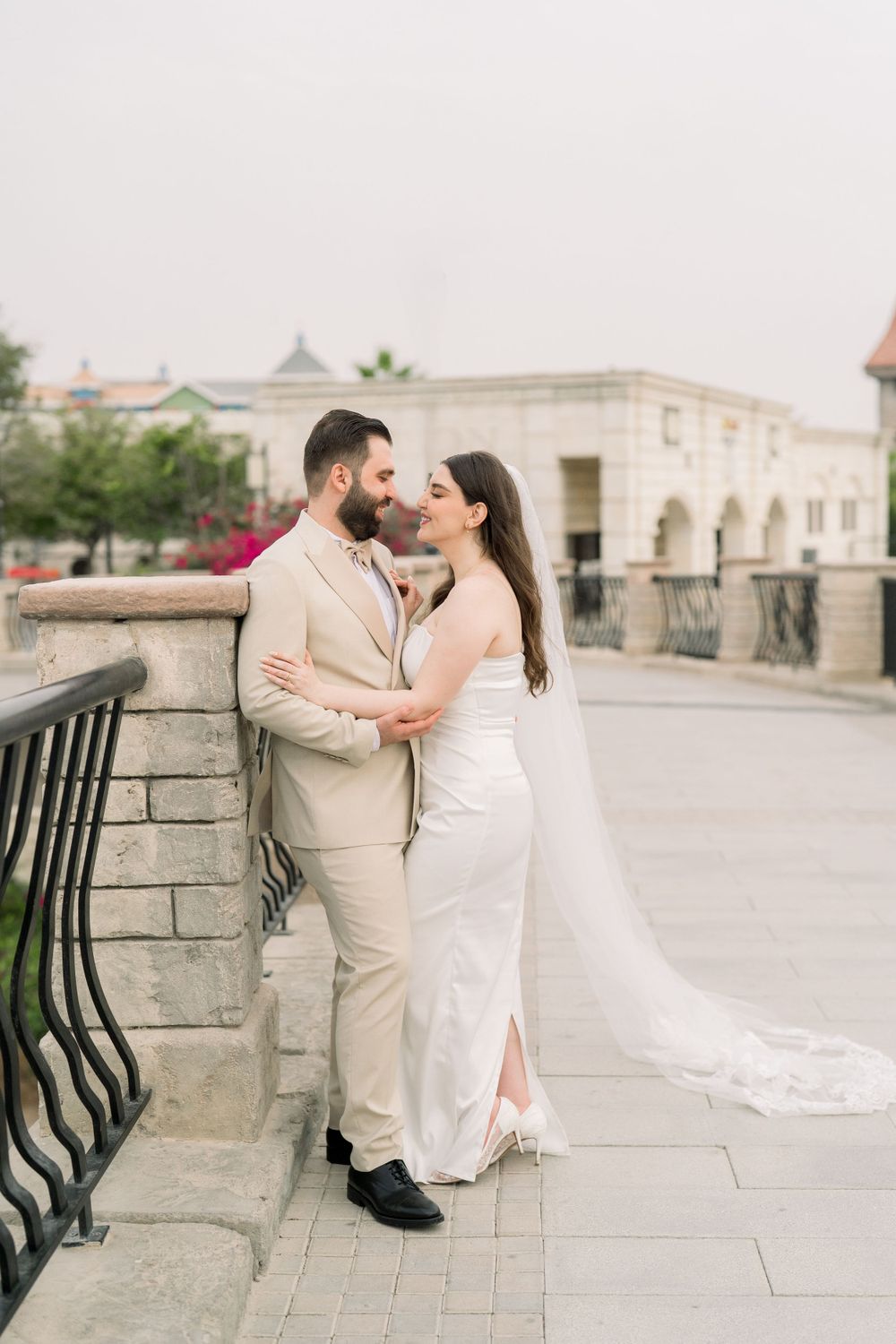 A romantic wedding couple embraces on a stone walkway near an elegant historic building.