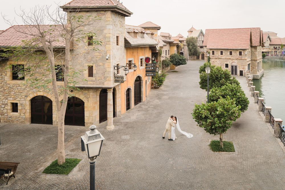 An aerial view of a Mediterranean-style village courtyard with stone buildings and ornate architecture along a waterfront.