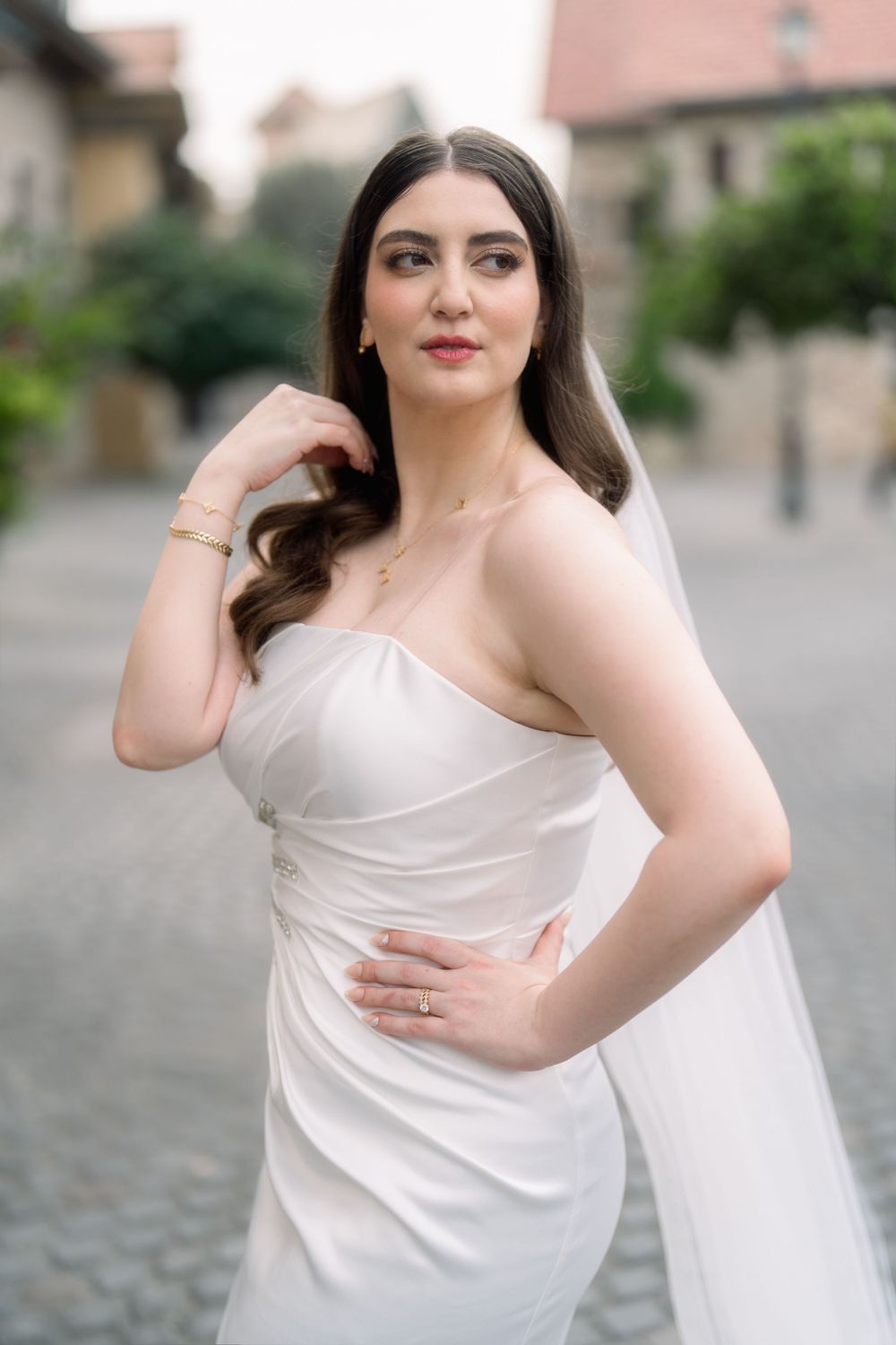 Beautiful bride in an elegant white strapless wedding gown poses outdoors on cobblestone street.