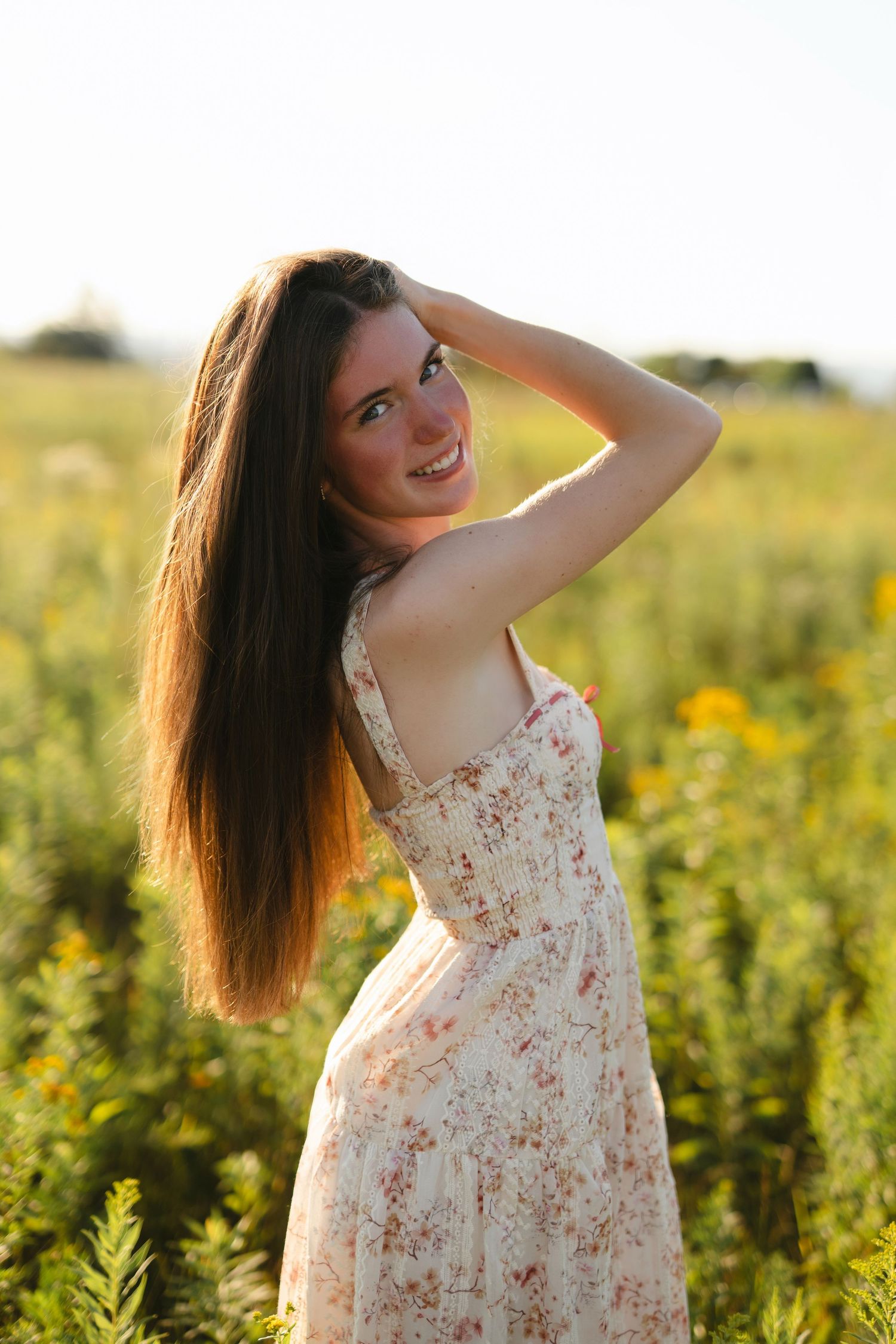 Someone in a white sundress poses in a golden wildflower field during sunset creating a dreamy summer portrait.