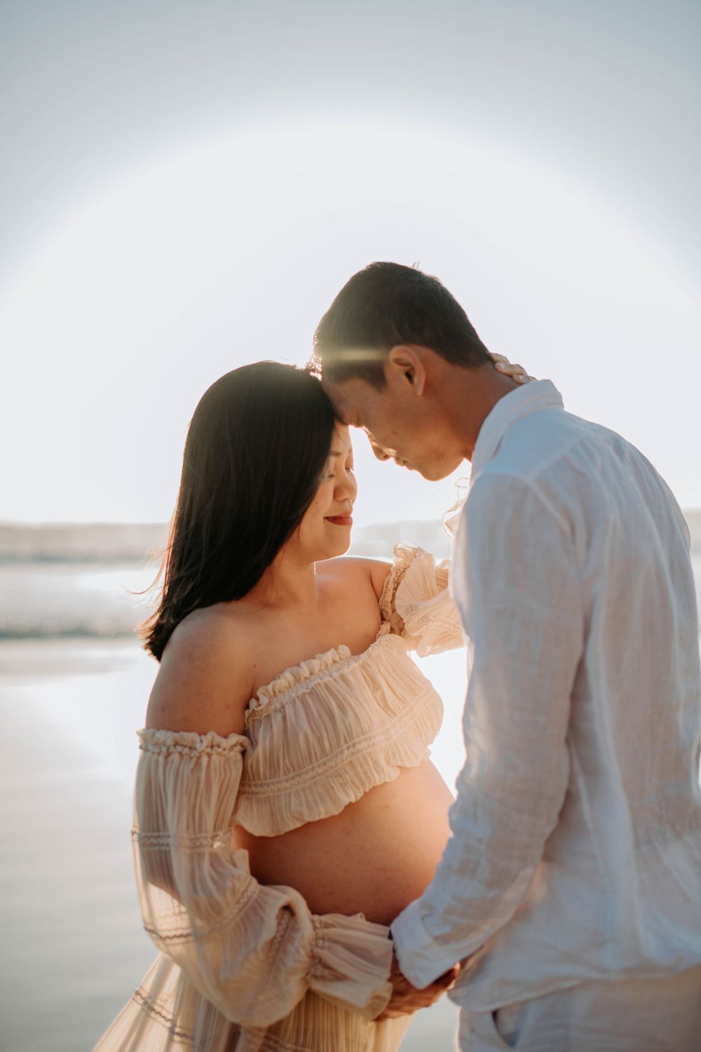 An intimate beach maternity photo capturing a tender moment at sunset.