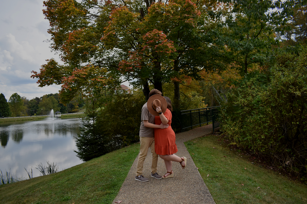 Couple embracing on walkway beside autumn lake at sunset.
