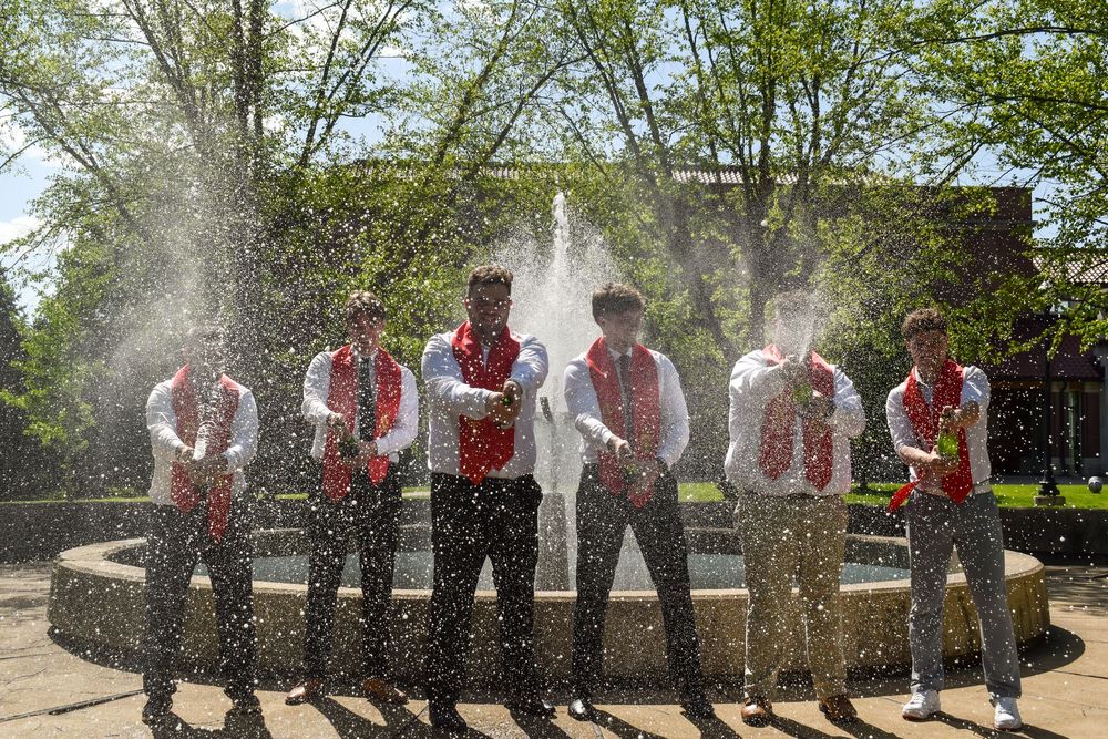 A group in traditional Bavarian attire splashes water in front of a fountain on a sunny day.