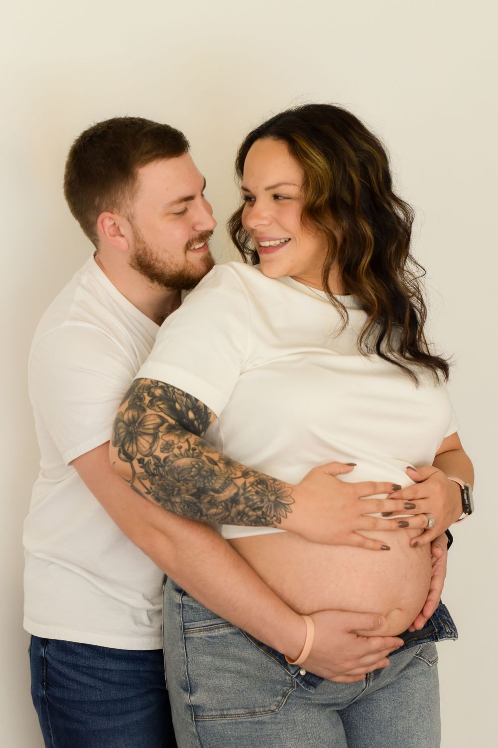 A couple in white shirts and jeans embraces intimately in a progressive series of affectionate poses against a neutral wall.