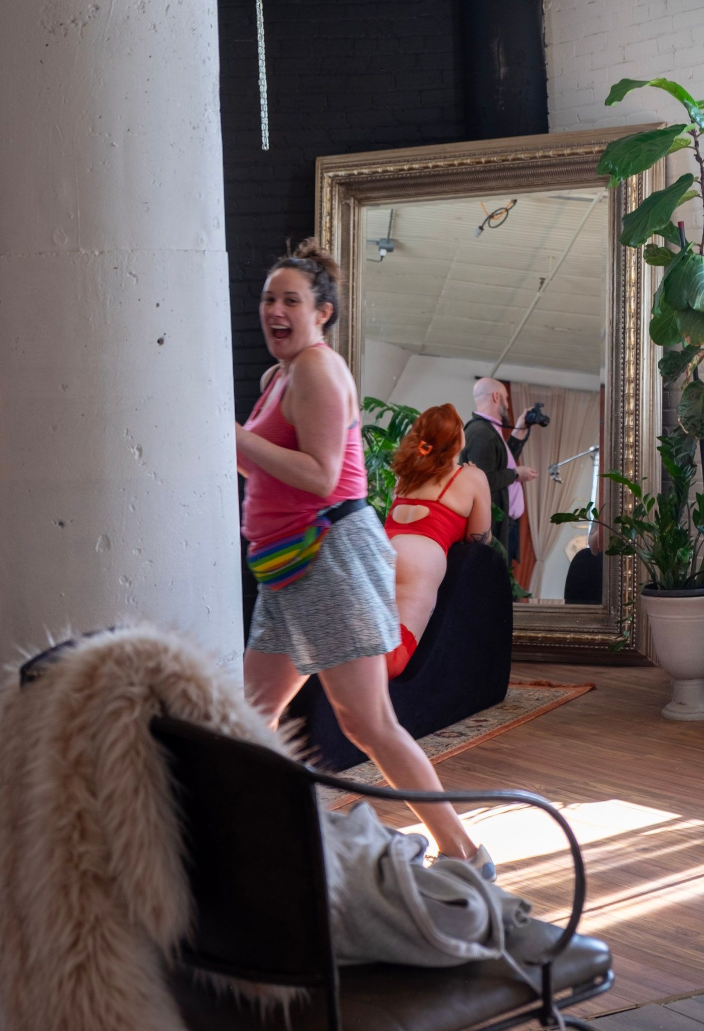 People in workout clothes dance and move energetically in a sunlit room with a large mirror and indoor plants.