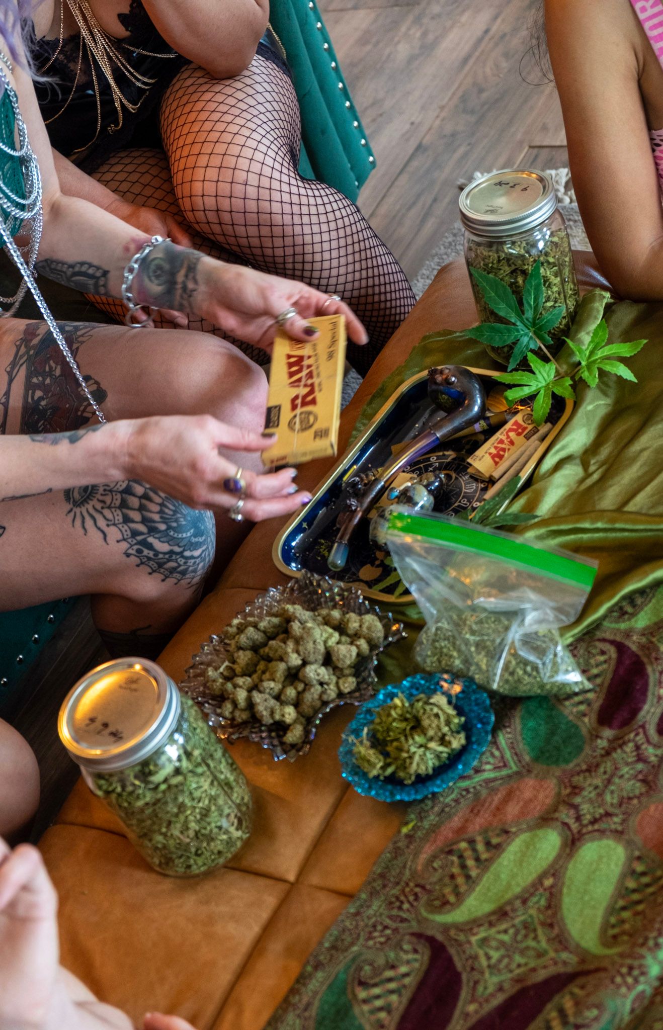Cannabis products and rolling papers arranged on a wooden floor with jars of marijuana and smoking accessories.