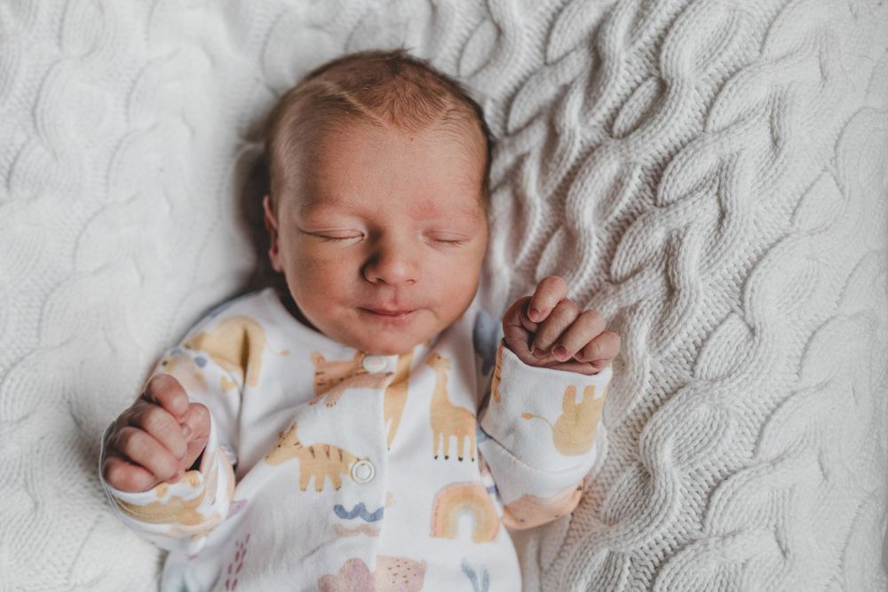 Peaceful sleeping newborn wearing animal print sleepwear rests on textured gray blanket.