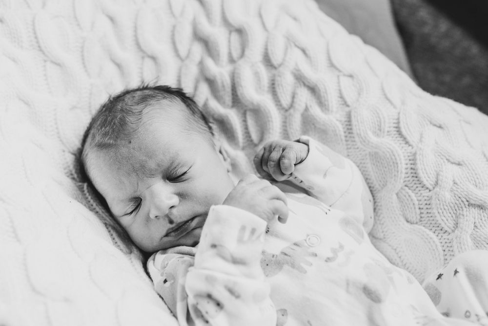 A sleeping newborn wearing white lies peacefully on textured white bedding in black and white photography.