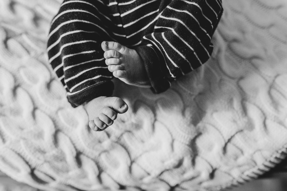 Close up black and white photo of tiny baby feet on a textured blanket showing adorable little toes.