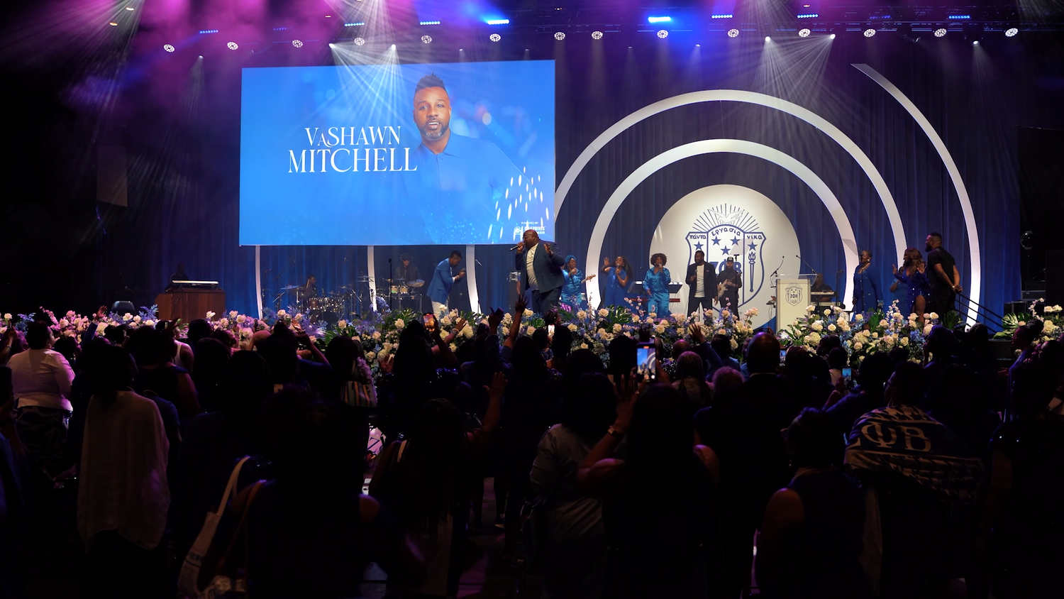 Large concert venue with circular stage design and blue lighting effects during a performance.