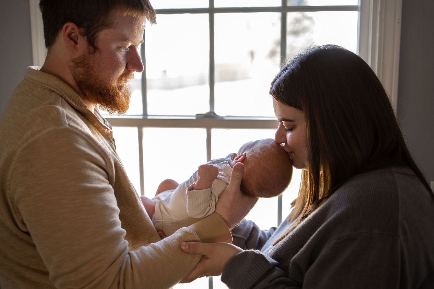 Springfield, IL Newborn Photographer captures a dad holding his newborn, while mom kisses his head during a lifestyle newborn session