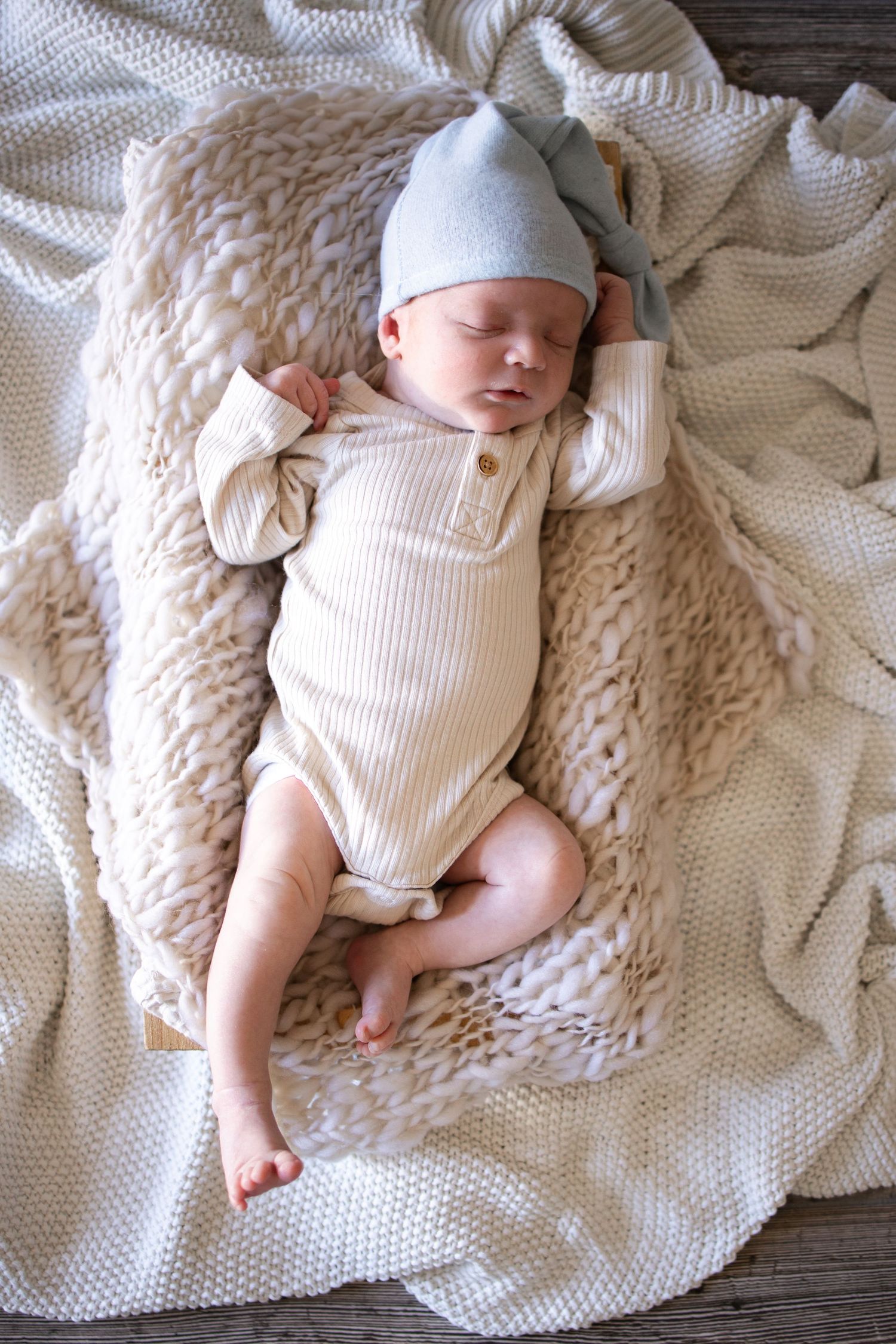 Springfield IL Newborn Photographer captures baby in a cream onesie with a blue hat laying in a basket during a lifestyle newborn session