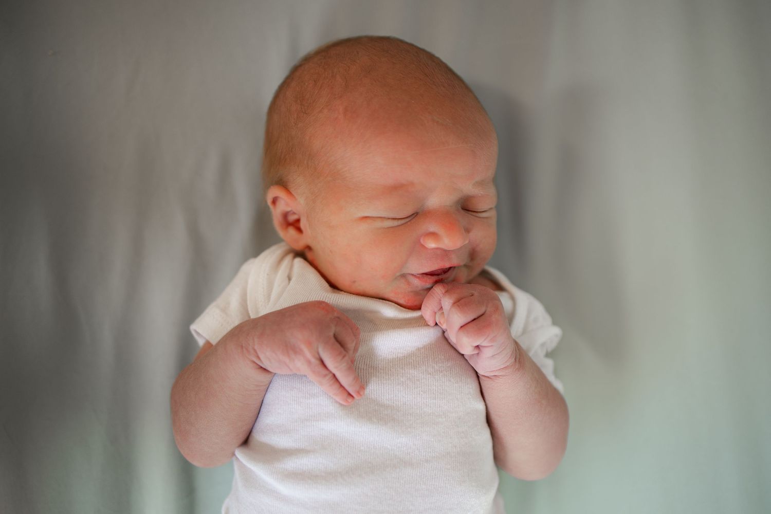 Springfield, IL Newborn Photographer | Newborn in a white onesie smiles while laying in his crib