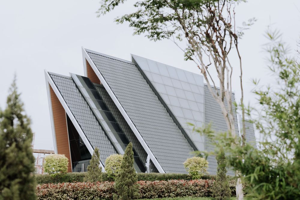 Modern house with multiple angular grey solar panels mounted on sloped surfaces surrounded by greenery.