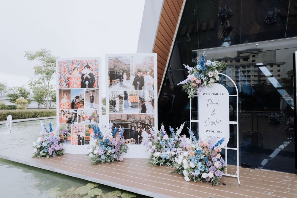 Wedding decor display with photo collage panels, white frame stand, and pastel blue floral arrangements on wooden deck.