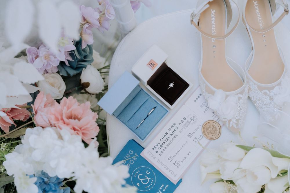 Wedding details flat lay with pink and white flowers, elegant bridal shoes, invitation suite and ring box in pastel colors.