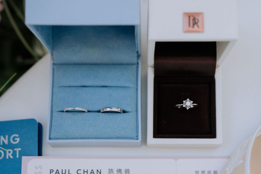 Two elegant engagement rings displayed in jewelry boxes, one in light blue and one in black velvet.