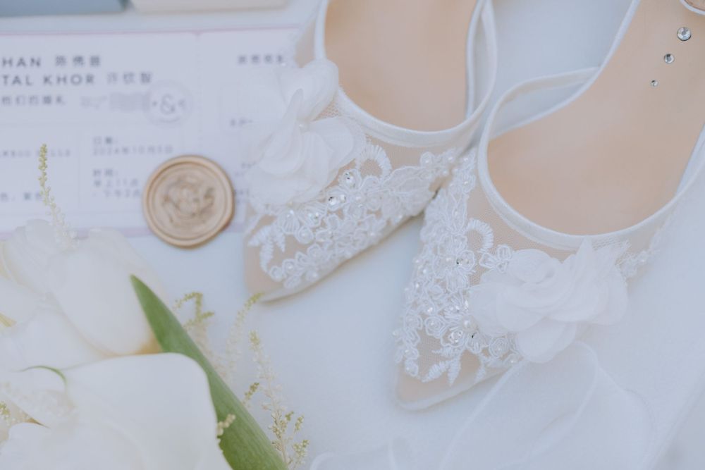 Elegant white lace wedding shoes photographed with floral details and a wax seal on a light background.