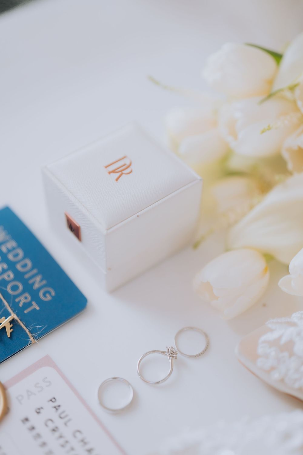 Wedding details with white ring box, wedding bands, and delicate white tulips arranged on a light surface.