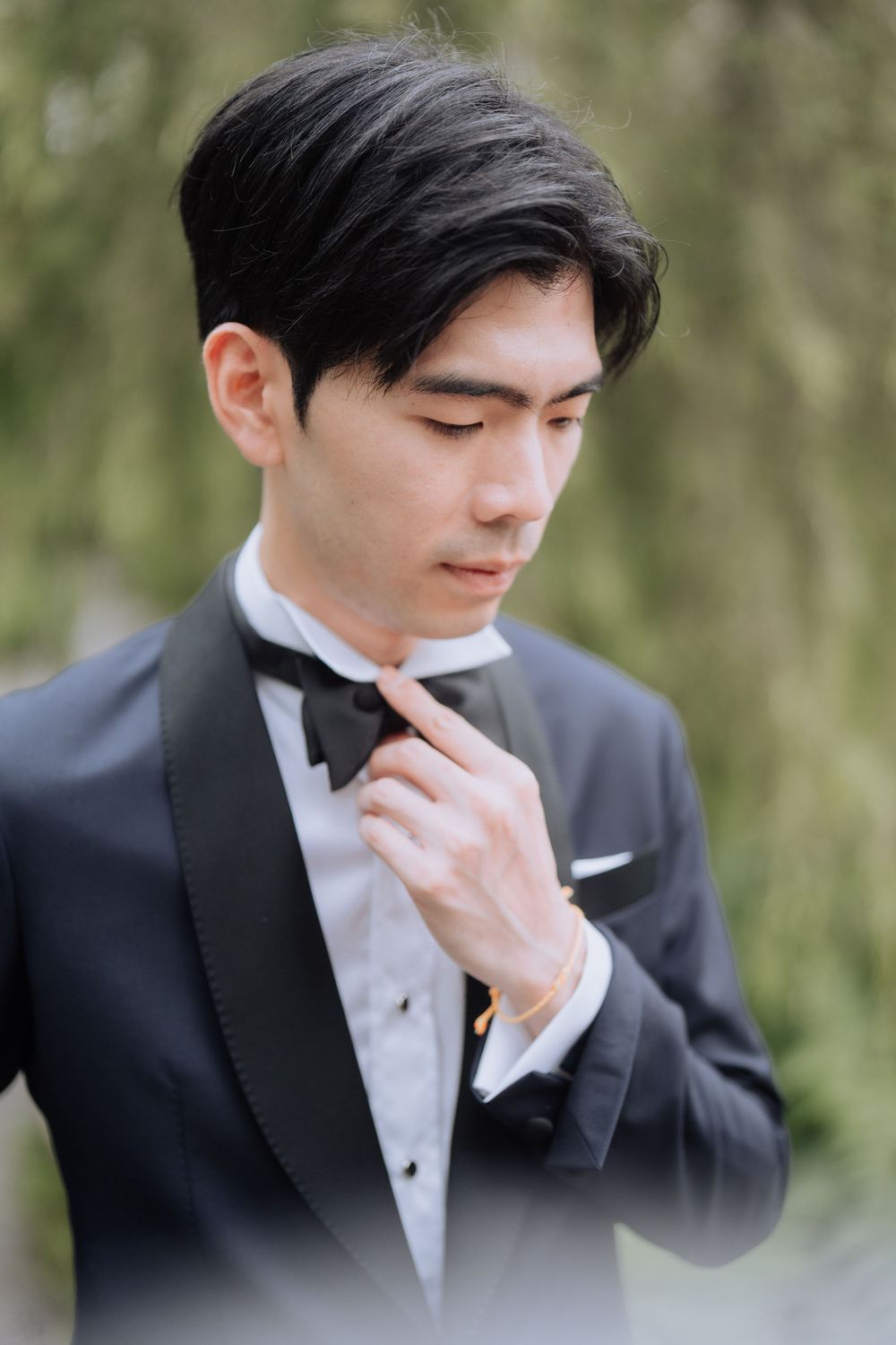 Elegant groom in classic black tuxedo and bow tie adjusts his collar outdoors.