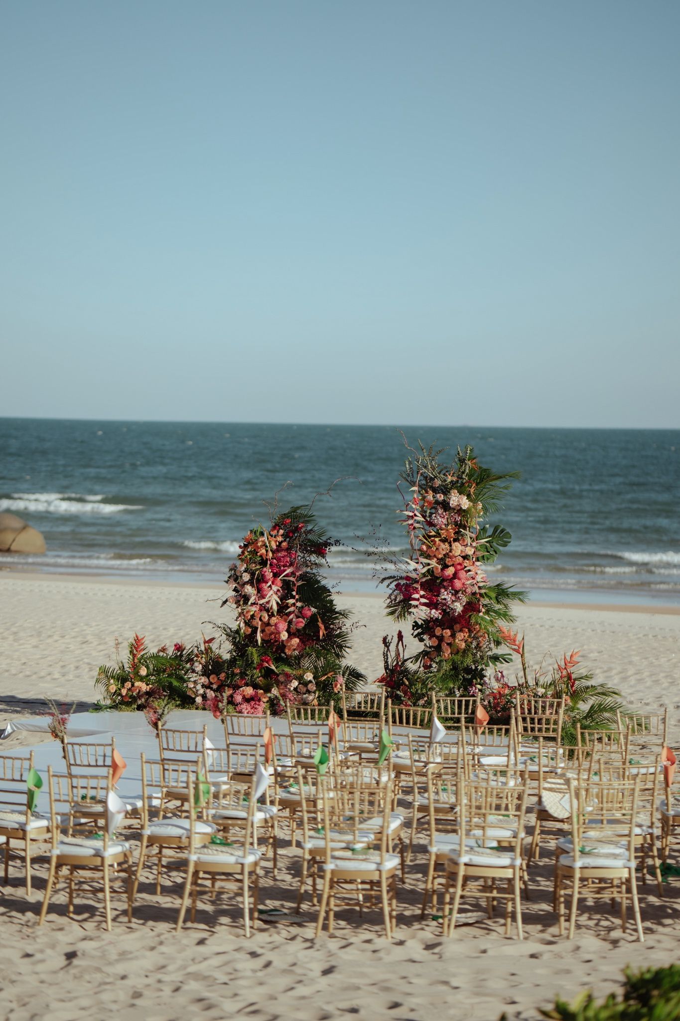 Tropical beach wedding ceremony with vibrant pink and orange floral arrangements by the ocean.