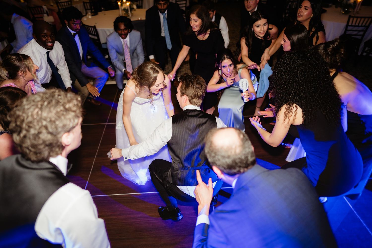 Wedding guests dancing in a circle on the dance floor at a lively reception party.