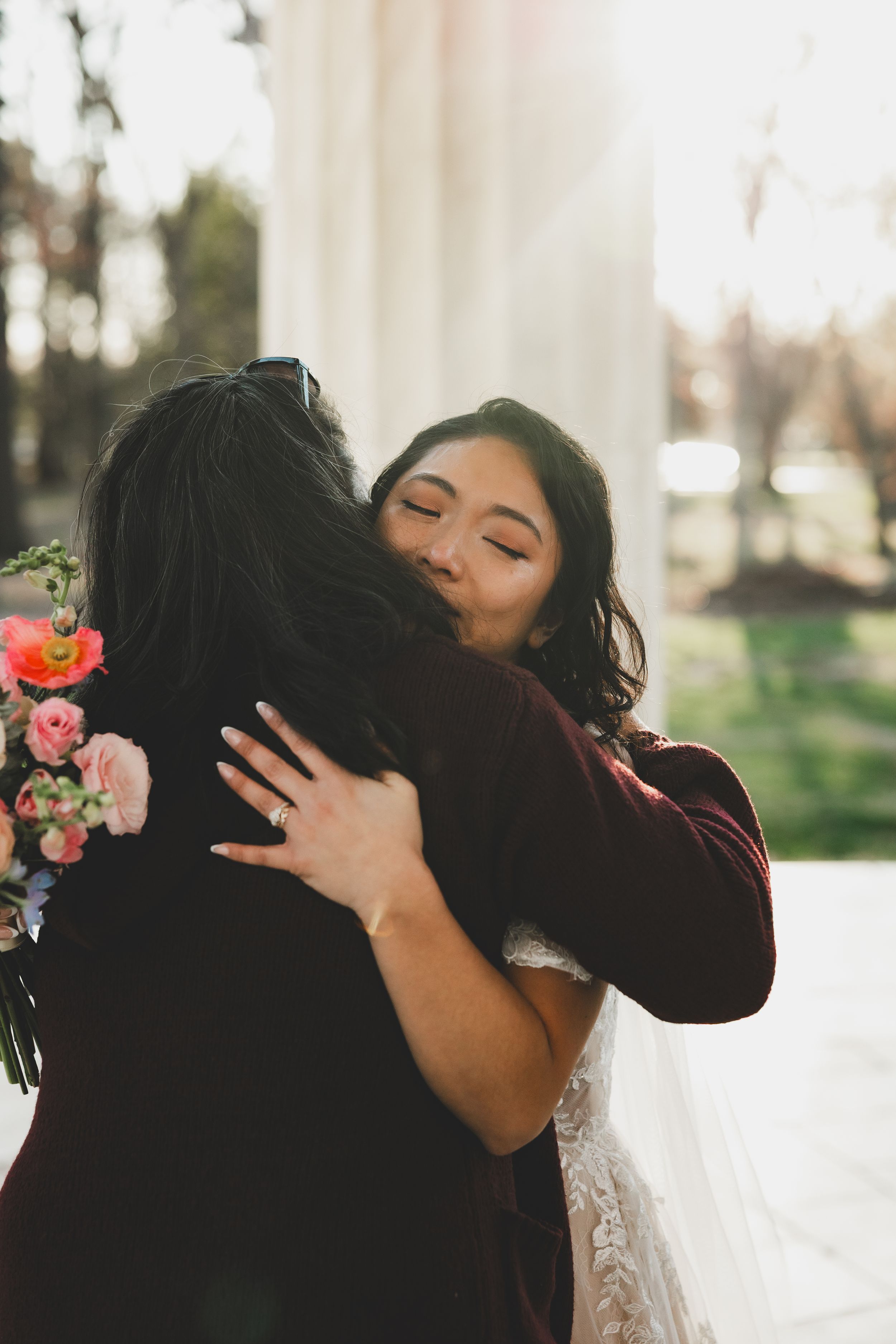 Bride smiling with eyes closed while sharing an emotional hug with a guest at her wedding ceremony.