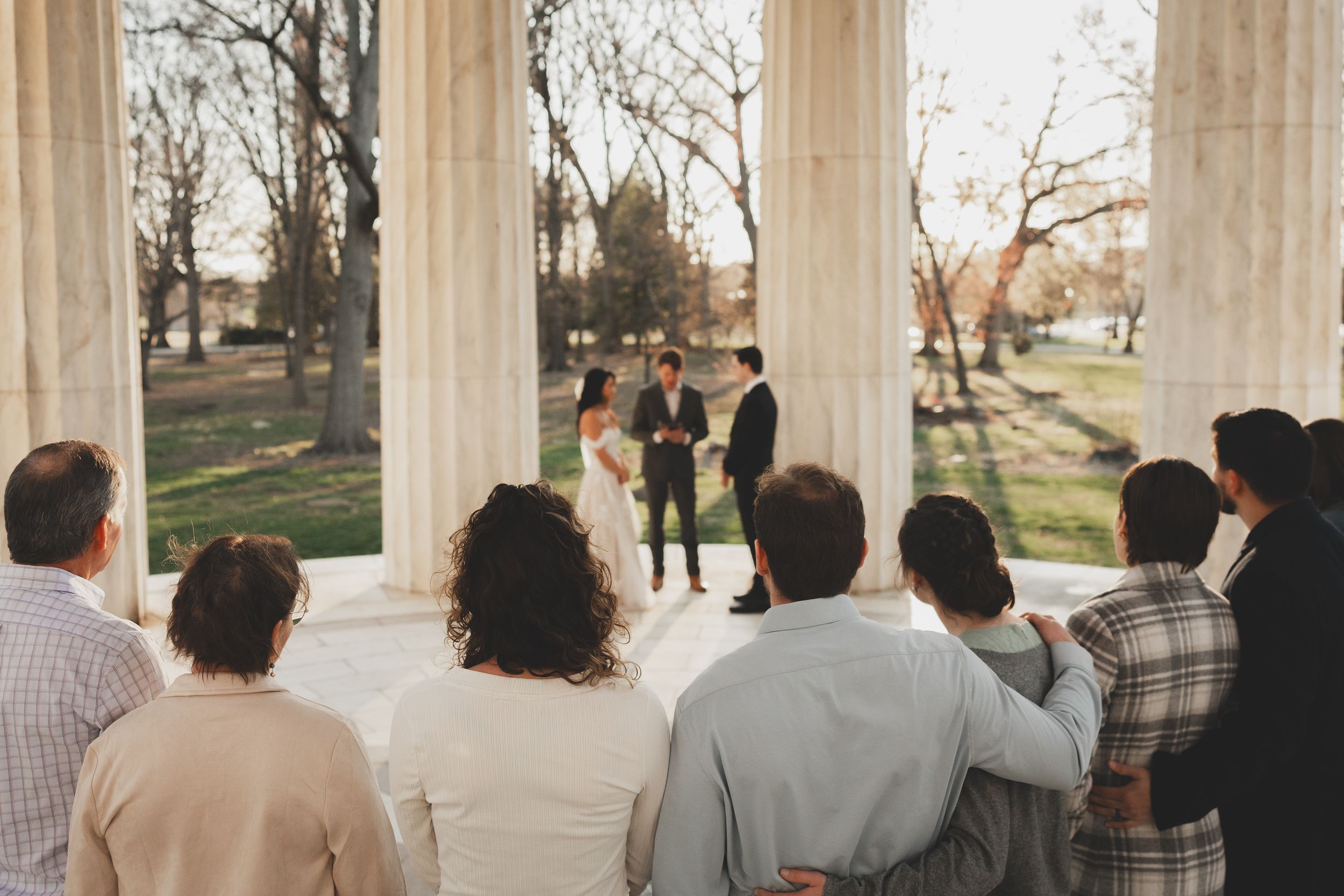 Small intimate wedding ceremony at the dc war memorial  with guests watching couple exchange vows outdoors.