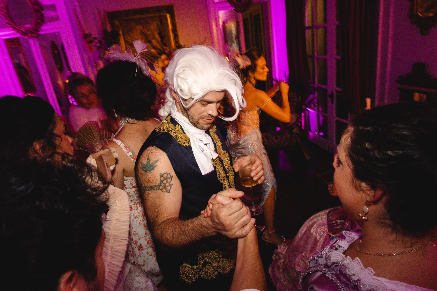 Man in colonial wig and vest dancing at a costume party with purple lighting.