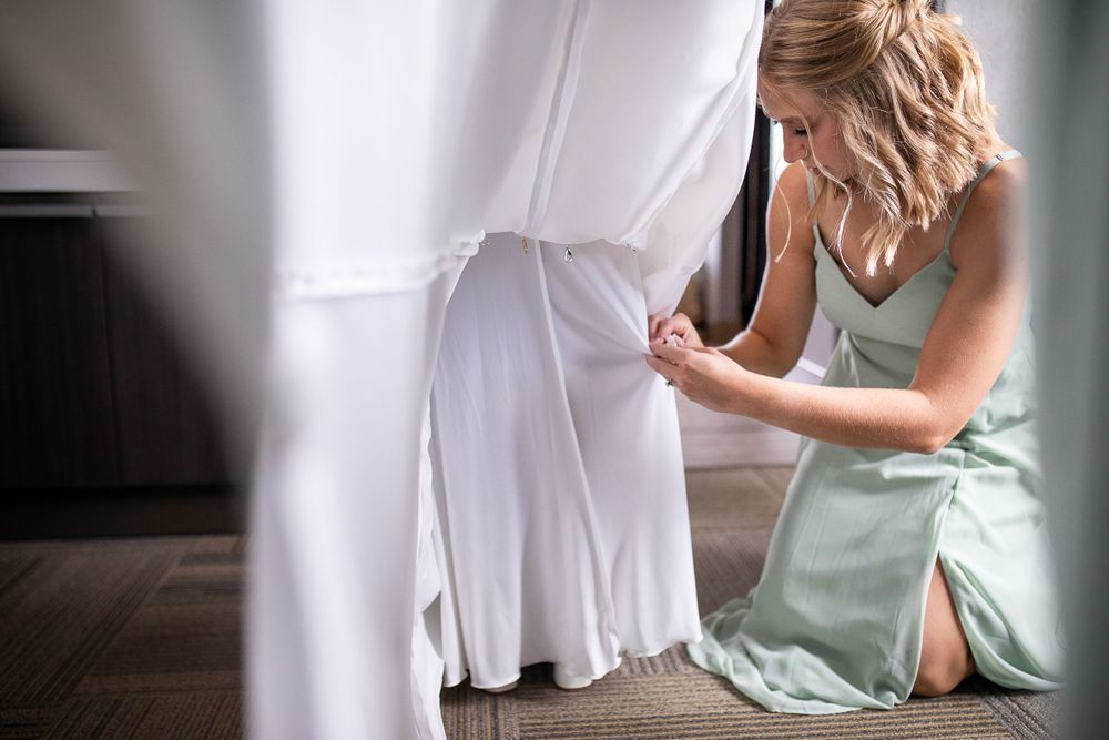 Someone in a mint green dress makes adjustments to a flowing white wedding gown during final preparations.  Iowa City wedding photographer.