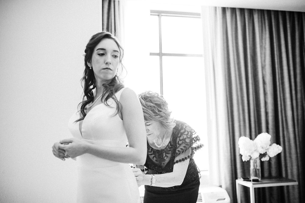 Black and white photograph showing final preparations and adjustments of a wedding dress in a sunlit room.  Iowa City wedding photographer.