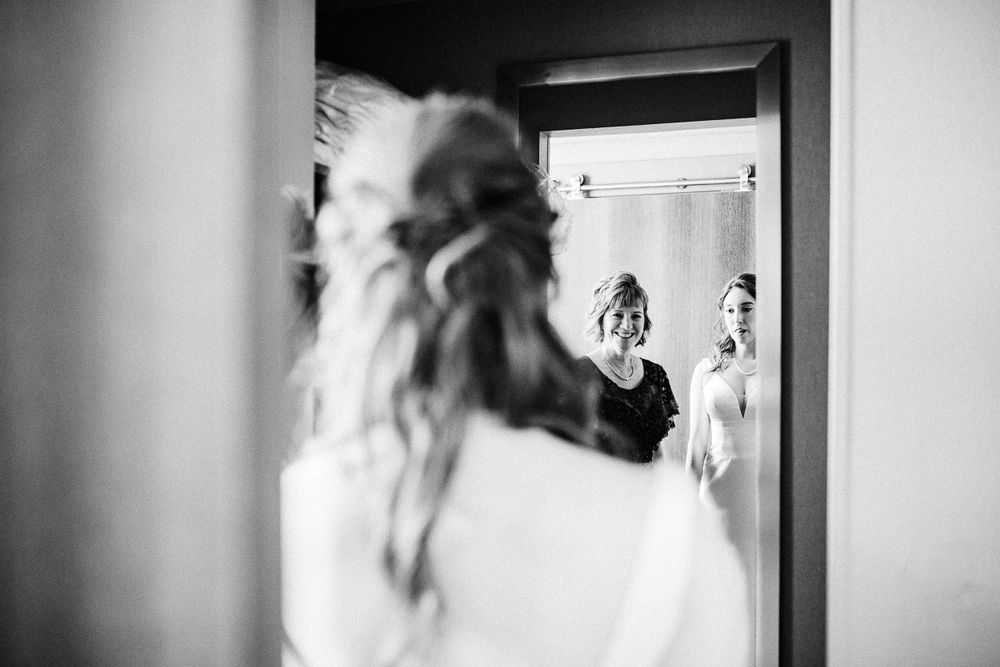Black and white photo showing a reflection in a mirror with two figures standing in a doorway.  Iowa City wedding photographer.