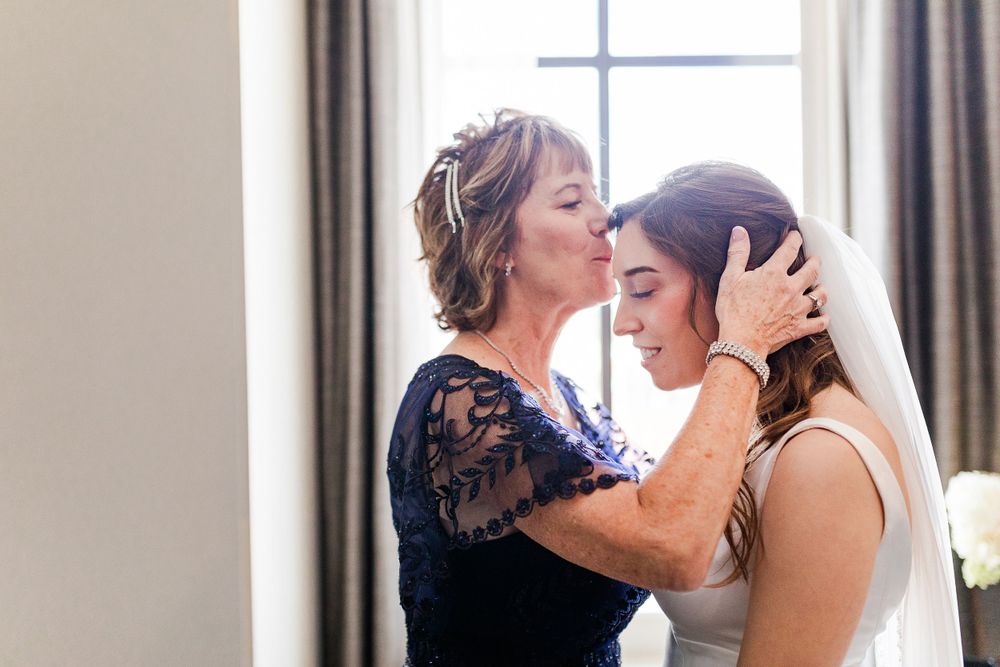 Tender moment between mom and daughter in formal attire by a window.  Iowa City wedding photographer.