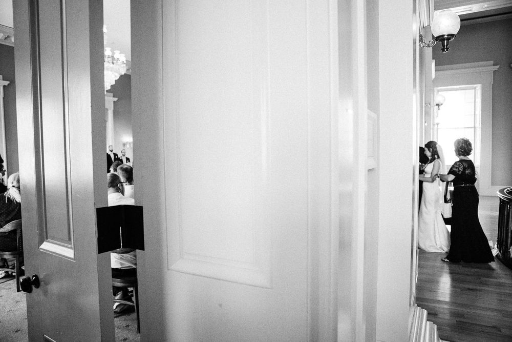 A black and white photograph showing people reflected in mirrors down a bright hallway corridor.  Iowa City wedding photographer.