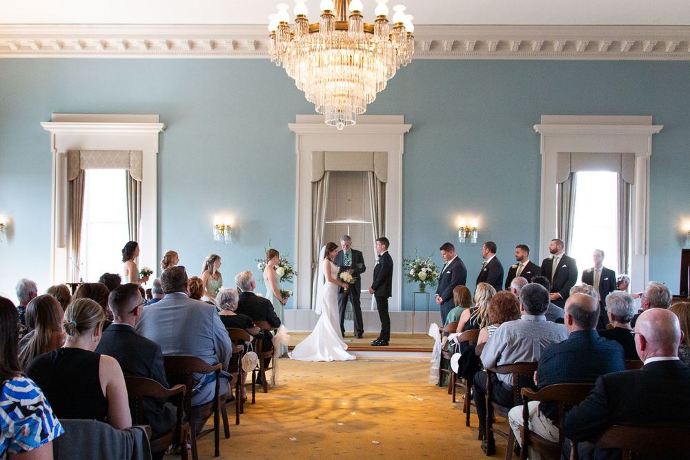 Wedding ceremony in an elegant room with crystal chandelier as guests watch the couple exchange vows.   Iowa City wedding photographer.