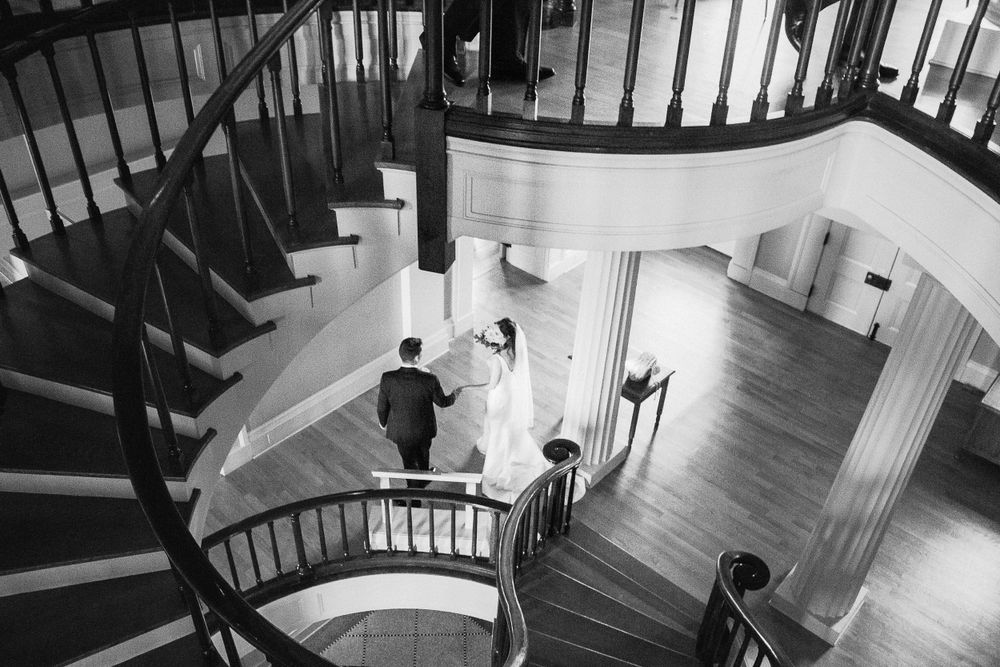 A black and white photo shows newleyweds descending an elegant curved staircase with wooden railings.   Iowa City wedding photographer.