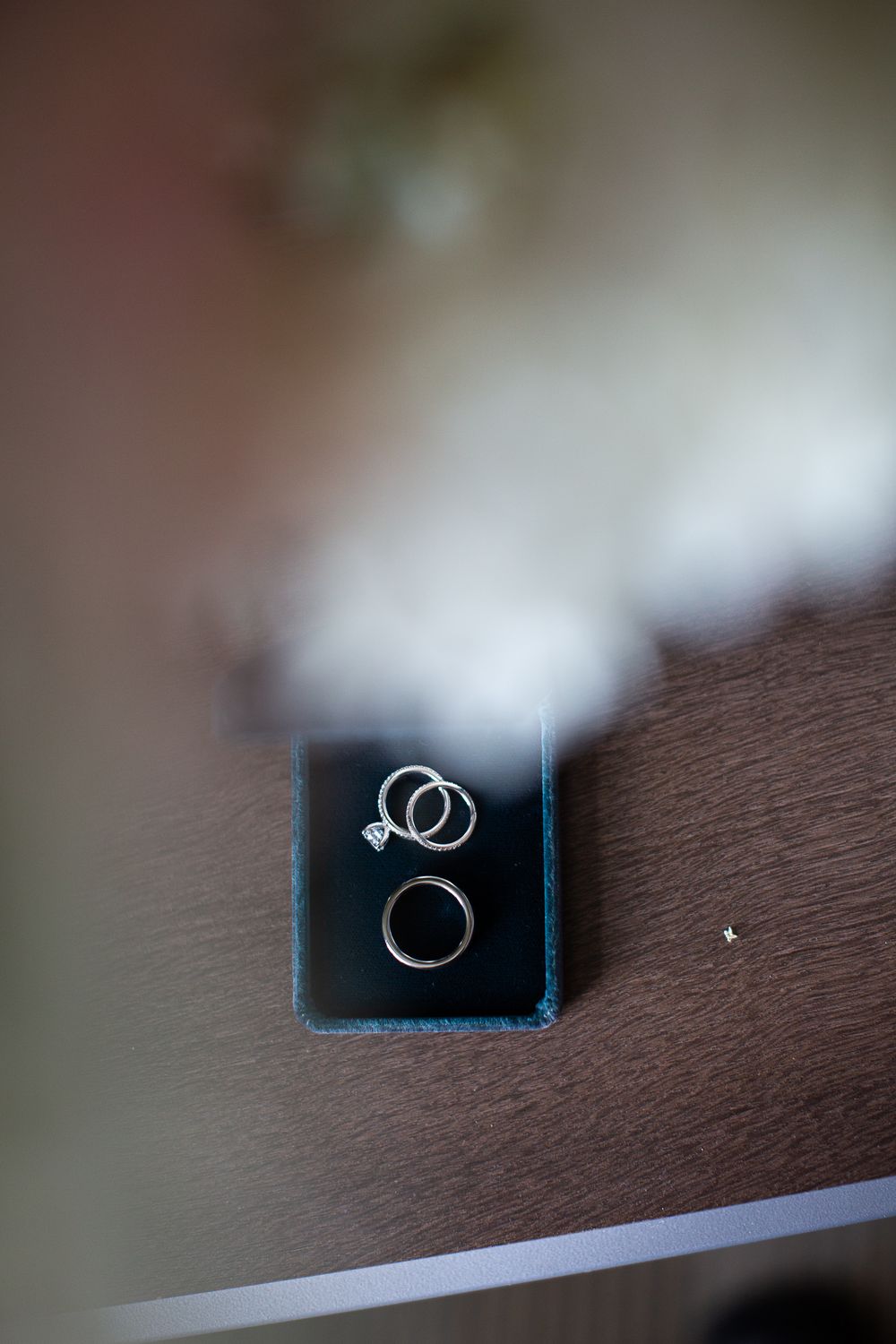 Wedding rings photographed on a dark teal velvet ring box against a wooden surface.  Iowa City wedding photographer.